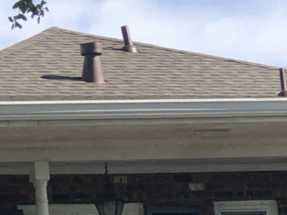 Roof with two brown vent pipes against a cloudy blue sky.