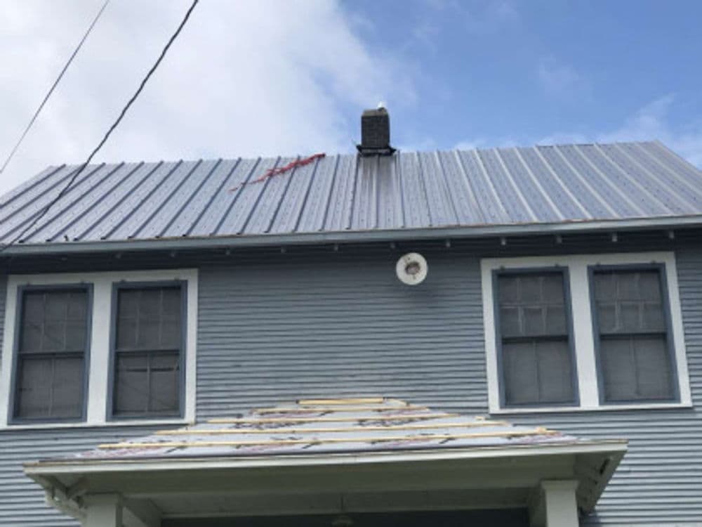 Damaged metal roof of a blue house with a chimney and repairs in progress.