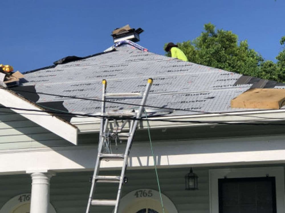 Worker installing a new roof on a house with a ladder and roofing materials visible.